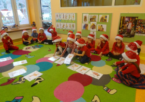 Grupa dzieci siedzi wokół ilustracji rozłożonych na dywanie, troje dzieci przekłada ilustrację.